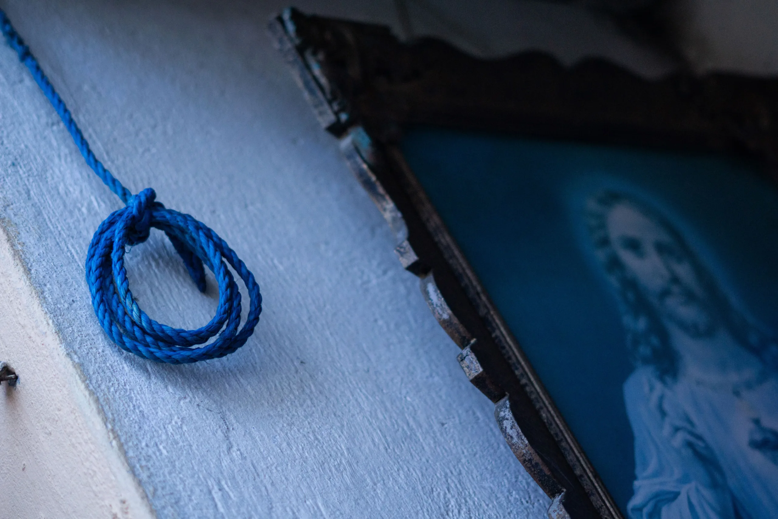 Una cuerda azul cuelga de una pared junto a una imagen de Jesucristo en un espacio interior. Foto: Nicolás Bernal.